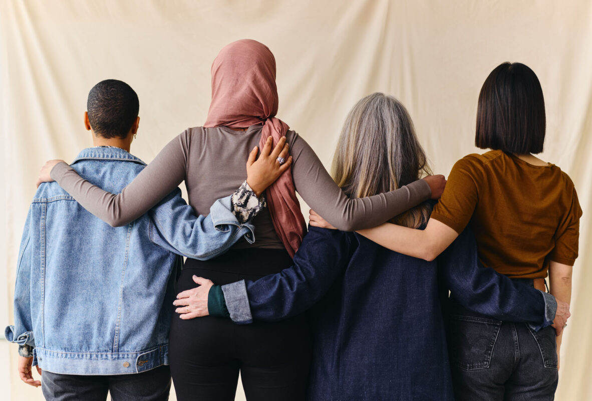 Rear View Of Four Women With Arms Around Each Other In Support O